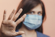 © fantom_rd - young woman in medical protective mask shows a stop gesture with hand on studio background, girl held out palm with fear, concept of quarantine measures
