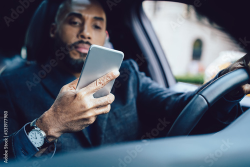 Calm adult ethnic man using smartphone in car