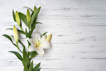 Composition Of White Lilies On A Light Wooden Background .