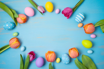 Wall Mural - Easter holiday background with easter eggs and tulip flowers on wooden table. Top view from above