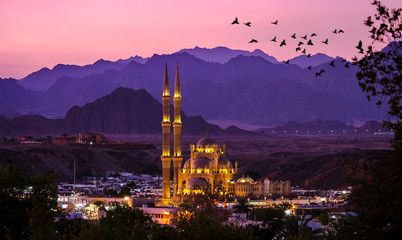 Al-Sahaba Mosque with night lights - arabic architecture and monuments in Sharm el Sheikh, Egypt. Ancient mosque of the old town at sunset with mountains silhouettes on skyline.