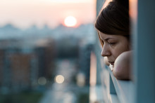 Young Sad Woman Looking Outside Through Balcony Of An Apartment Building