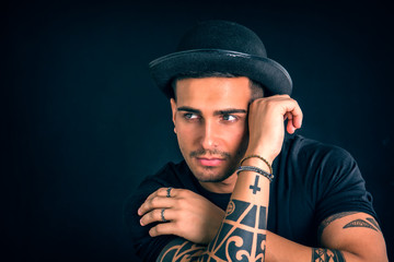 Wall Mural - Handsome and stylish young man with black bowler hat and t-shirt. Cool tattoos on arms