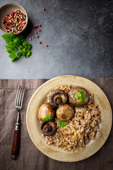 Wall Mural - Buckwheat porridge with mushrooms in a plate on black background, top view