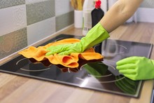 Woman hand in gloves polishing hob glass with microfiber cloth