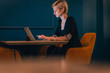 © qunica.com - Confident young businesswoman working on her laptop while sitting in a corner of a cafe with dark blue walls.
