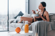 © standret - Young woman with slim body shape in sportswear sits on sofa and eats healthy diet food indoors at home