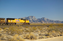 Freight Train Travels Through Desert And Mountainous Areas Of Mojave Desert In Southern California