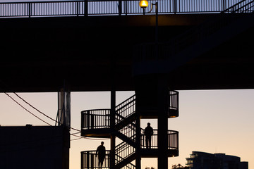 Silhouettes of two men on an outdoor spiral staircase in the city during evening blur hour.