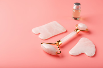 A set of tools for face Massage technique Gua Sha made of natural rose quartz on a pink background. Roller, jade stone and oil in a glass jar for face and body care.