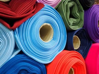 Rolls of bright multicolored fabric close-up. Coils of fabric are on the shelves in the store. Sample of coat cotton fabric in rolls