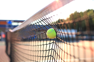 Bright greenish yellow tennis ball hitting the net.