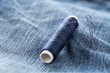 Blue yarn thread with needle on blue jeans denim close up - jeans fashion mending or repair concept