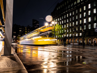 A dynamic night scene showing a Metrolink tram captured with a slow shutter outside St Peter's Square in Manchester, UK