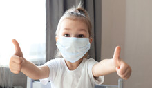 Little Girl In A Medical Mask Showing Thumb's Up Gesture. Protection Against Coronavirus.