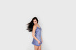 © aleksissay - Beautiful young woman with long straight dark hair in blue silk nightdress on grey background. Womans hair in move. Female turns and looks down. Beauty and fashion concept. Copy space for text.