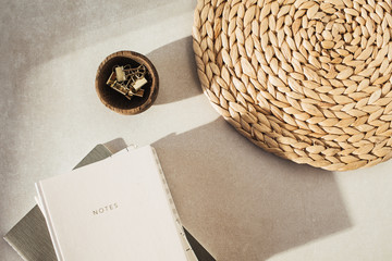 Notebooks, clips in wooden bowl, straw stand on beige concrete background. Office desk workspace. Business, work blank template. Flat lay, top view.