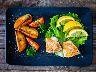 Fish dish - fried cod fillet with vegetables on wooden table