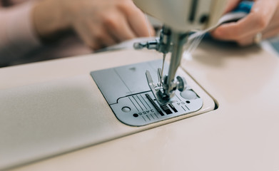 Woman hands using the sewing machine to sew the face home made diy medical mask during the coronavirus pandemia.