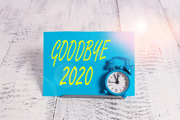 Wall Mural - Handwriting text Good Bye 2020. Conceptual photo express good wishes when parting or at the end of last year Mini blue alarm clock stand tilted above buffer wire in front of notepaper