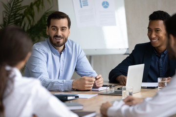 Smiling multiracial businesspeople sit at desk discuss cooperation with business partners clients, happy diverse colleagues talk brainstorm at office meeting together, teamwork, partnership concept