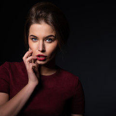 Leinwandbilder - Portrait of attractive young woman over black background. Amazing girl with perfect makeup wearing elegant deep red dress. Beauty and fashion