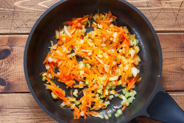 Step by step cooking vegetable stew with cauliflower, step 2 - frying carrots, onions, celery in a pan, top view, selective focus