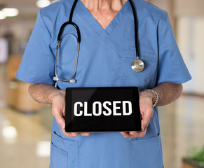 Senior male caucasian doctor with stethoscope in medical scrubs holding electronic tablet for saying hospital is closed due to coronavirus