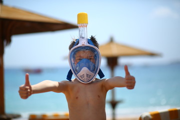 Portrait of a happy caucasian boy at the seaside wearing a diving mask and showing like gesture