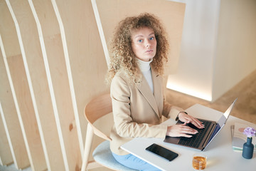Wall Mural - High angle portrait of modern curly haired young woman looking at camera while using laptop sitting at table in cafe, copy space