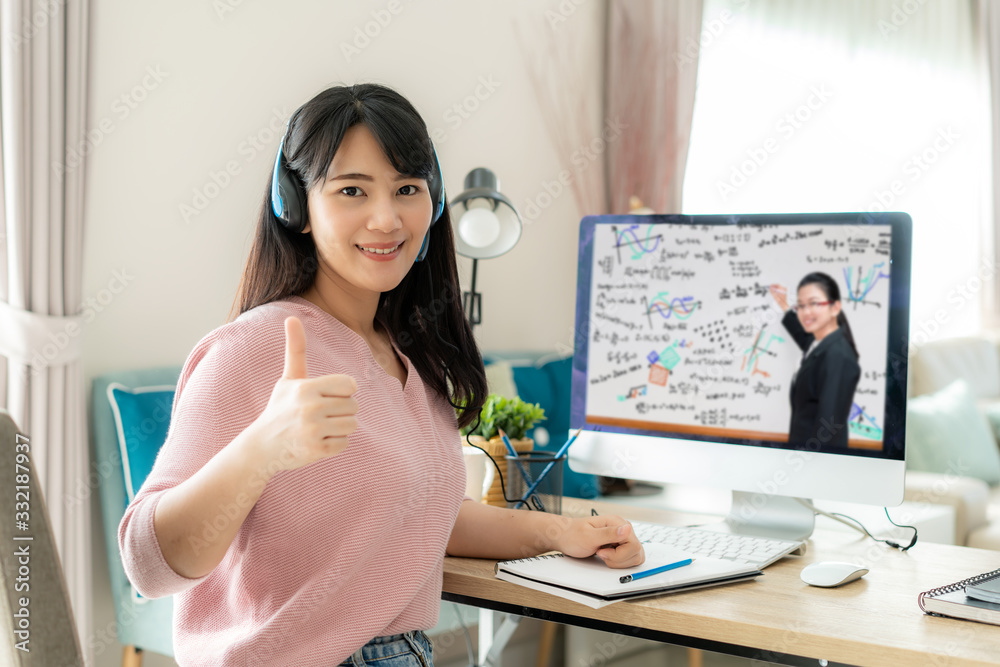 Asian woman student video e-learning with teacher on computer and thumb up in living room at home. E-learning ,online ,education and internet social distancing protect from COVID-19 viruses. - obrazy, fototapety, plakaty 