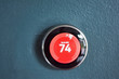 Nest smart home thermostat with red center in heat mode. Saving energy heating home. Isolated product on blue wall