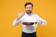 Smiling young bearded male chef cook or baker man in white uniform isolated on yellow background. Cooking food concept. Mock up copy space. Holding frying pan, raised hand to face, feeling food smell.