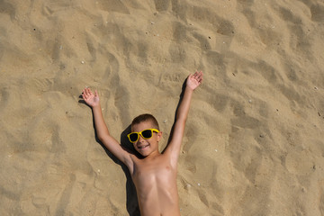 Little boy in sunglasses on the beach. Child in swimming trunks on the sea sand.