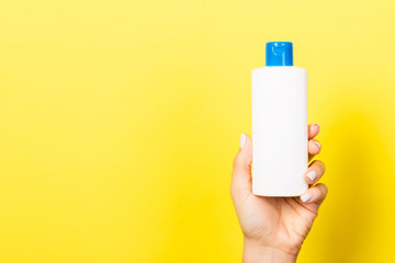 Yellow background with woman's hand holding a cosmetics bottle with copy space