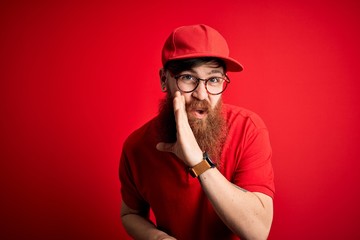 Canvas Print - Young handsome delivery man wearing glasses and red cap over isolated background hand on mouth telling secret rumor, whispering malicious talk conversation