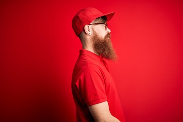 Canvas Print - Young handsome delivery man wearing glasses and red cap over isolated background looking to side, relax profile pose with natural face and confident smile.