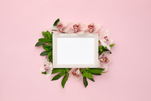 Photo Frame Decorated With Green Leaves And Orchid Flowers On Pink Pastel Background. Empty Space For Text. Mock Up With Copy Space. Flat Lay