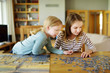 © MNStudio - Cute young girls playing puzzles at home. Children connecting jigsaw puzzle pieces in a living room table. Kids assembling a jigsaw puzzle. Fun family leisure.