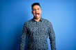 © Krakenimages.com - Young handsome man wearing casual shirt standing over isolated blue background sticking tongue out happy with funny expression. Emotion concept.