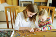 © MNStudio - Cute young girls playing puzzles at home. Children connecting jigsaw puzzle pieces in a living room table. Kids assembling a jigsaw puzzle. Fun family leisure.
