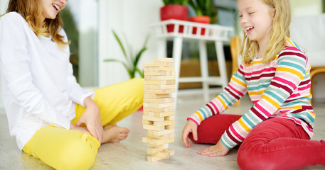 Wall Mural - Two sisters playing wood blocks tower game at home. Kids practicing their physical and mental skills. Fun board games for family leisure. Stay at home activity for kids.