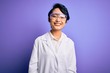 © Krakenimages.com - Young beautiful asian scientist girl wearing coat and glasses over purple background with a happy and cool smile on face. Lucky person.