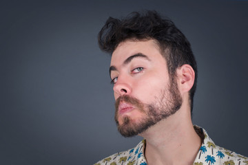 Beautiful man with snobbish expression curving lips and raising eyebrows, looking with doubtful and skeptical expression, suspect and doubt. Standing indoors over gray background.