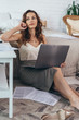 © undrey - Pensive woman sits on the floor with a laptop at home