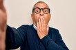 © Krakenimages.com - Senior handsome grey-haired man wearing sweater and glasses making selfie by camera cover mouth with hand shocked with shame for mistake, expression of fear, scared in silence, secret concept