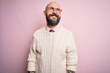 Sticker - Handsome bald man with beard and tattoo wearing glasses and sweater over pink background looking away to side with smile on face, natural expression. Laughing confident.