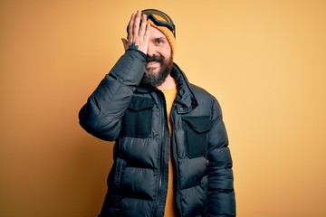 Poster - Handsome skier bald man with beard skiing wearing snow sportswear and ski goggles covering one eye with hand, confident smile on face and surprise emotion.