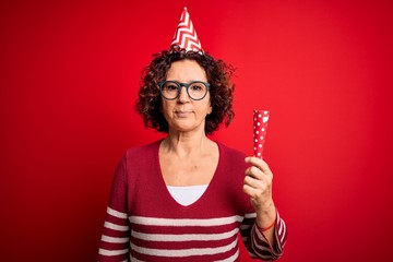 Poster - Middle age curly hair woman wearing birthday funny hat holding party trumpet on celebration with a confident expression on smart face thinking serious