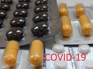 Covid-19 inscription on the background of black and white tablets, yellow capsules. Concept of treatment of dangerous Asian coronavirus.